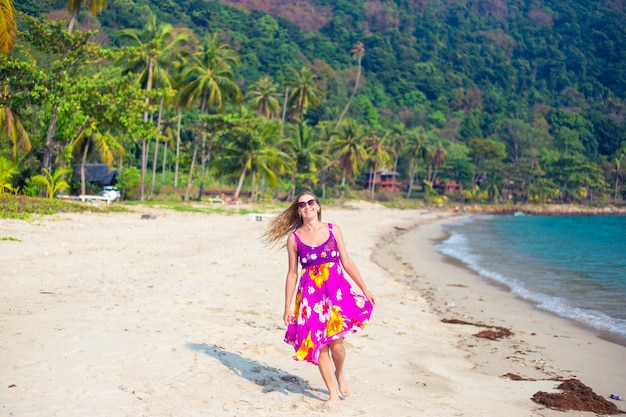Une femme blonde adulte dans une robe lumineuse sur un bord de mer tropical rit. Voyage et tourisme.