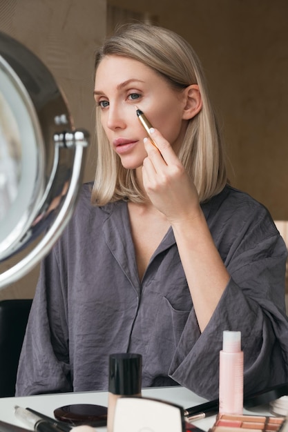 Femme blonde adulte maquillant et utilisant un conciliateur Regarde dans le miroir assis à la maison La vie de luxe