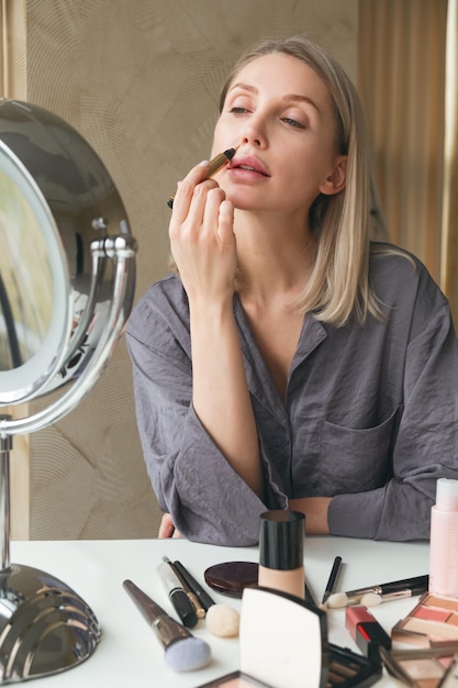 Femme blonde adulte maquillant et utilisant un conciliateur Regarde dans le miroir assis à la maison La vie de luxe