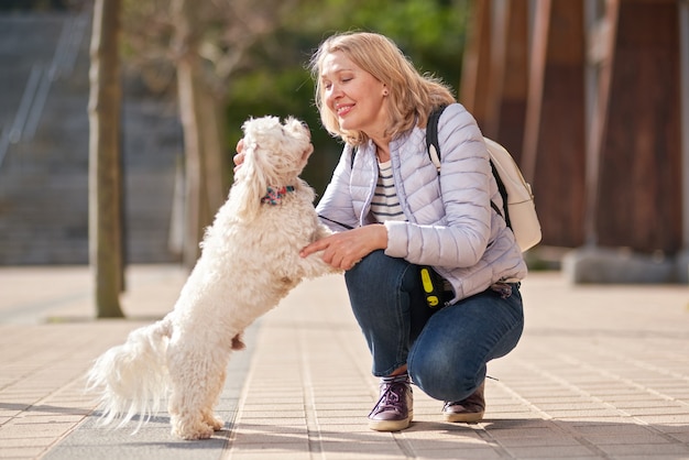 Femme blonde adulte marchant avec un chien blanc moelleux dans la ville d'été.