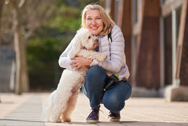 Femme blonde adulte marchant avec un chien blanc moelleux dans la ville d'été.