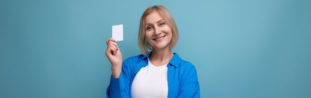 Femme blonde d'âge moyen avec une coupe de cheveux bob tenant une carte de crédit sur un fond de studio