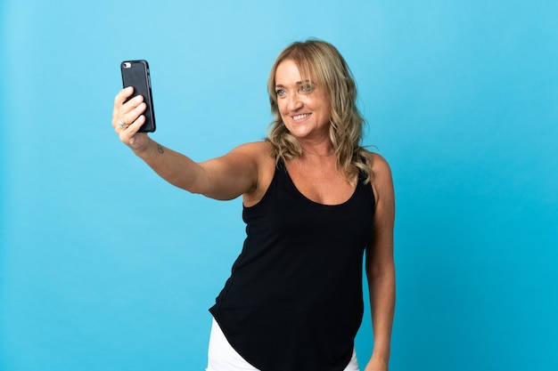 Femme blonde d'âge moyen sur fond isolé faisant un selfie