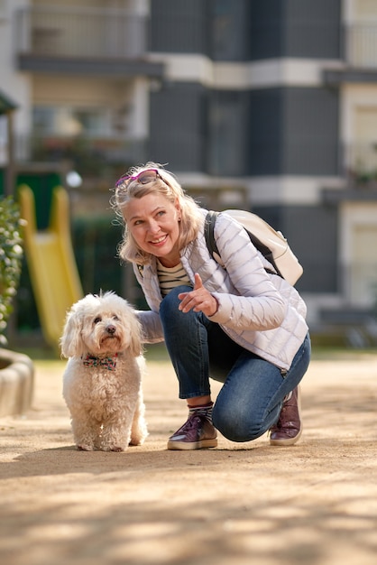 Femme blonde d'âge moyen marchant avec un chien blanc moelleux dans la ville d'été.