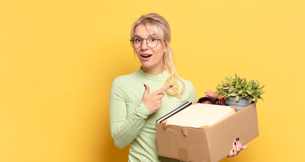 Femme blonde à l'air excité et surpris pointant vers le côté et vers le haut pour copier l'espace