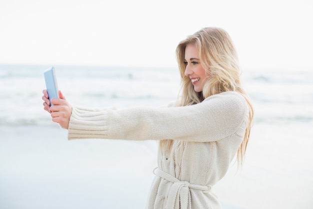 Femme blonde amusée en cardigan de laine prenant une photo d&#39;elle avec un tablet pc