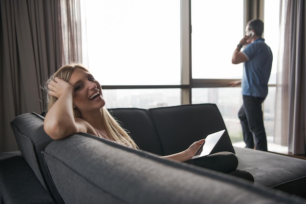 Femme blonde assise sur un canapé à l'aide de sa tablette