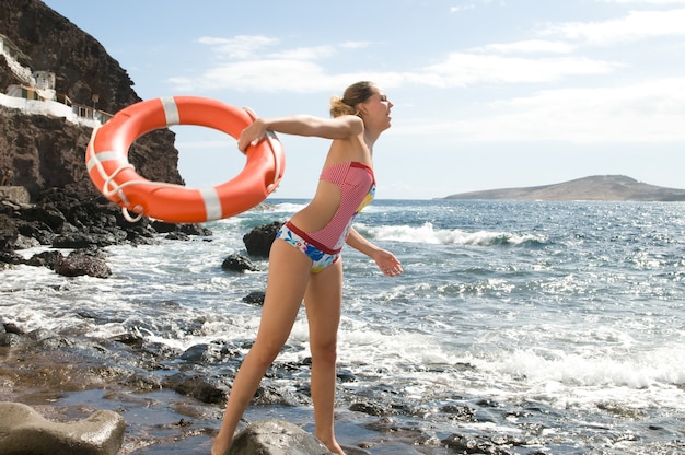 femme blonde au bord de la mer avec une bouée de sauvetage près des vagues