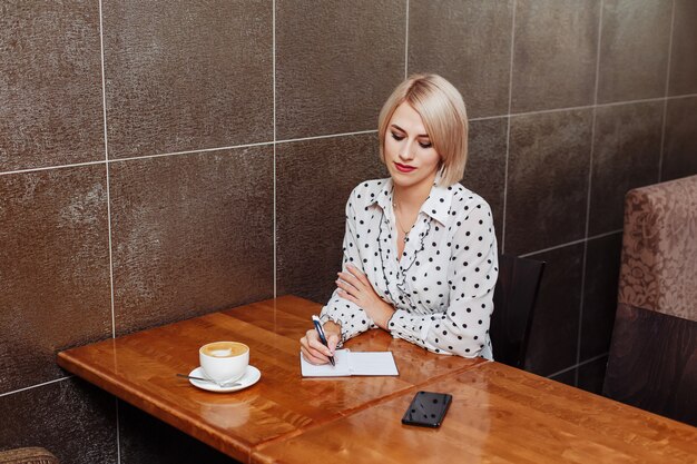 Femme blonde au café écrit dans le cahier