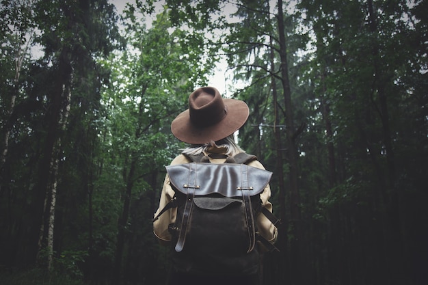Femme blonde au chapeau avec sac à dos en jour de pluie dans la forêt