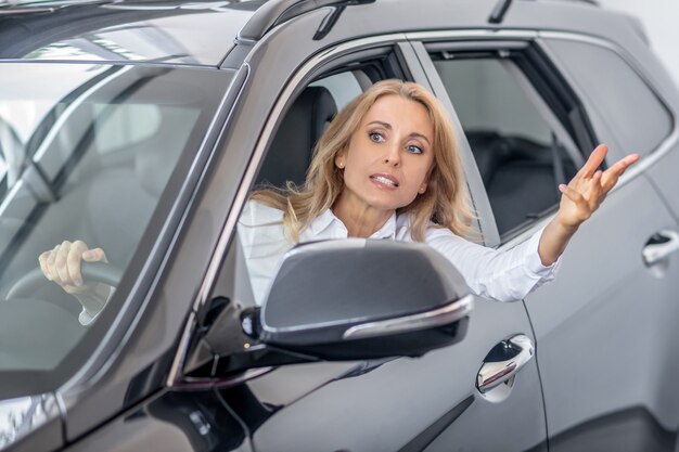 Femme blonde au volant d'une voiture et gesticulant vigoureusement