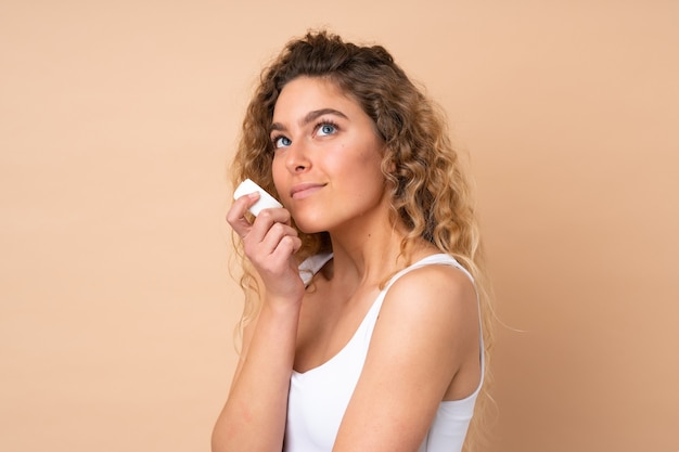 Femme blonde aux cheveux bouclés isolé avec une crème hydratante et le sentir