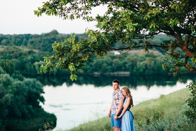 Femme blonde aux cheveux dénoués dans une robe bleu clair et un gars à la lumière du coucher de soleil dans la nature