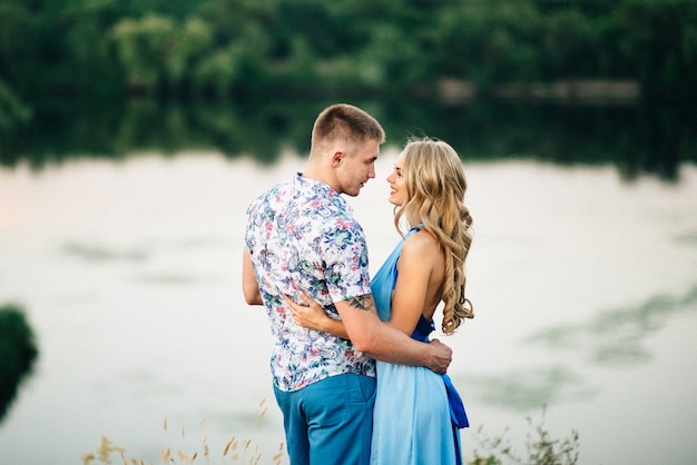 Femme blonde aux cheveux dénoués dans une robe bleu clair et un gars à la lumière du coucher de soleil dans la nature