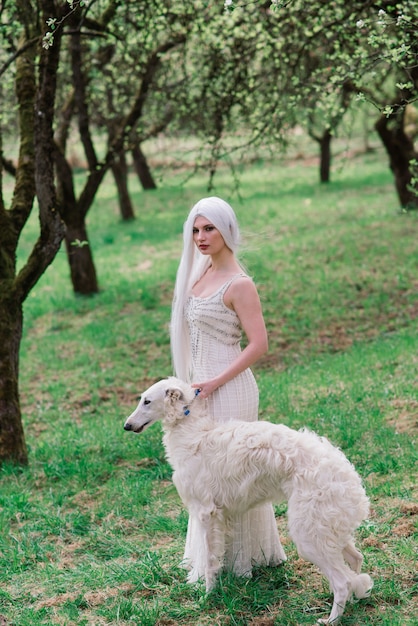 Femme blonde aux cheveux longs jouant avec son chien lévrier russe dans le jardin