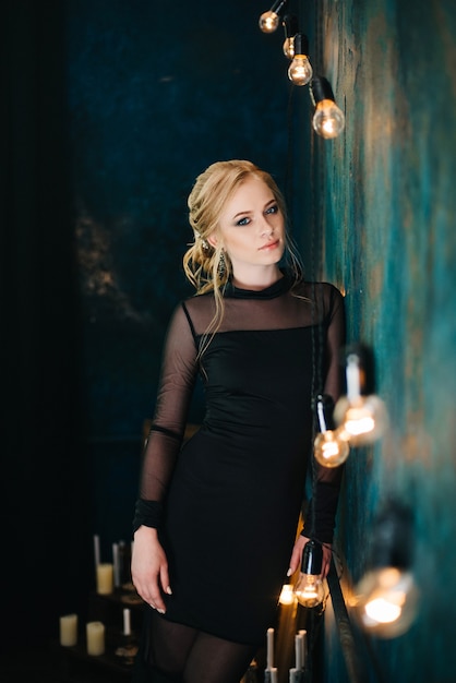 Femme blonde aux yeux bleus dans une robe noire dans un intérieur turquoise foncé