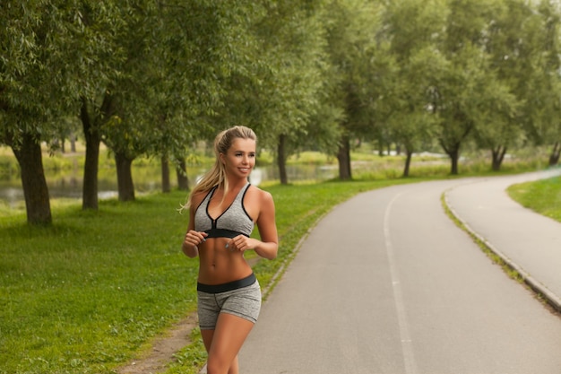 Femme blonde belle remise en forme en mode sport wear course et pratique le yoga dans le parc au coucher du soleil