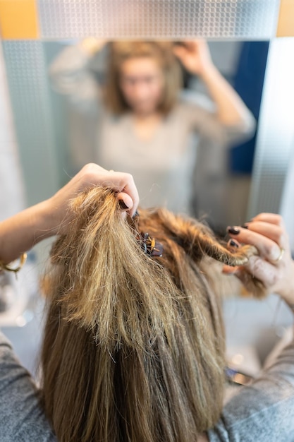 Femme blonde et blanche devant le miroir et fixant ses cheveux pour les peigner et les brosser