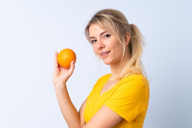 Femme blonde sur bleu isolé tenant une orange