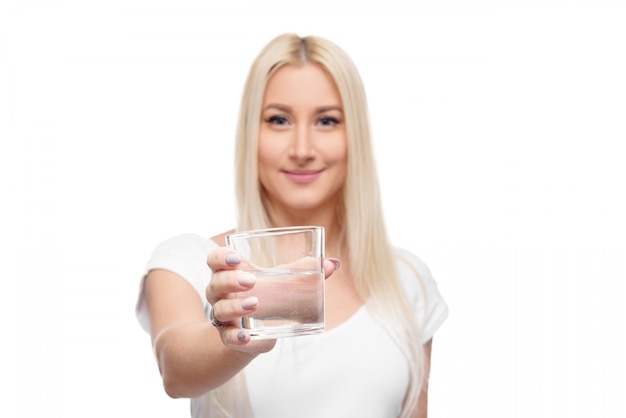 Femme blonde en bonne santé tenant et boire un verre et une bouteille d'eau pure sur fond blanc isolé