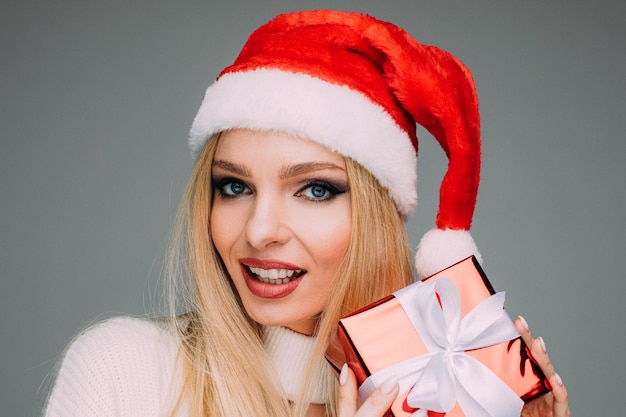 femme blonde en bonnet de Noel rouge tient un petit cadeau