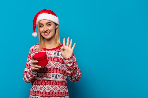 Femme blonde avec Bonnet de Noel souriant et à la convivialité, montrant le numéro quatre ou quatrième avec la main en avant, compte à rebours