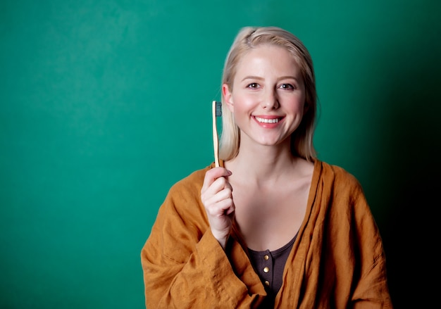 Femme blonde avec une brosse à dents en bois sur scène verte