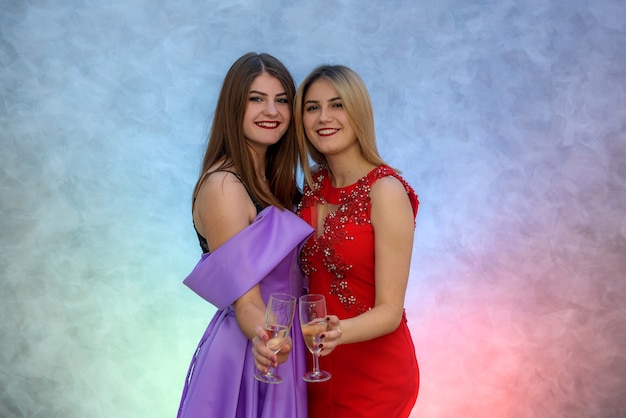 Femme blonde et brune en robes de soirée élégantes posant avec des verres à champagne