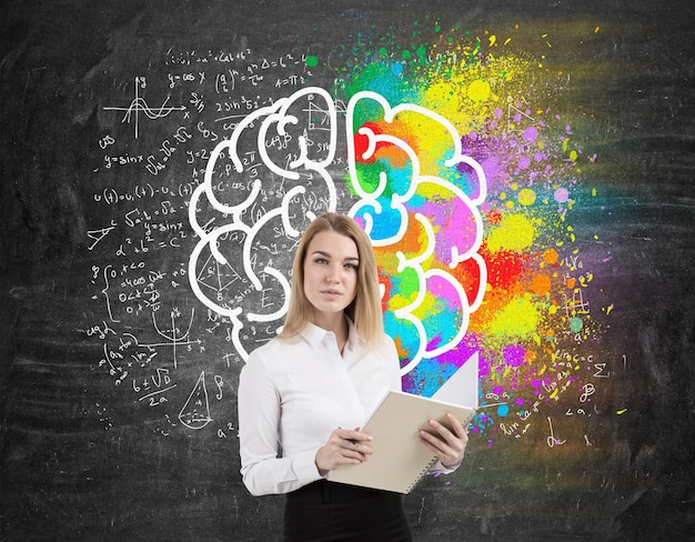 Femme blonde avec un cahier près d'un tableau avec un croquis coloré du cerveau