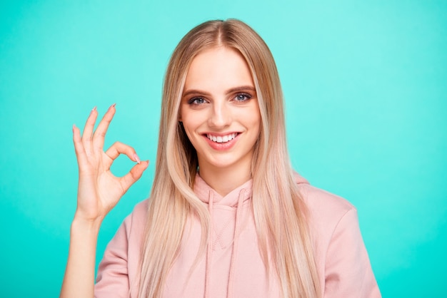 Femme blonde avec capuche rose posant contre le mur bleu