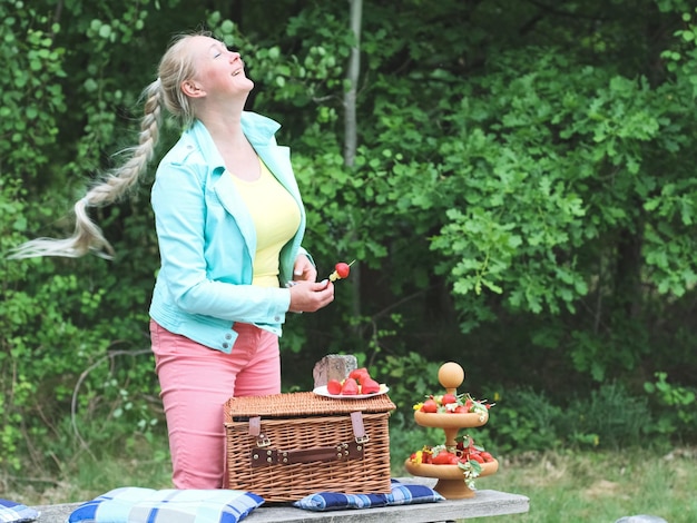 Une femme blonde caucasienne heureuse avec un sourire agite une longue faux tout en préparant un barbecue aux fruits
