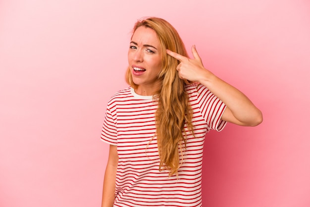 Femme blonde caucasienne isolée sur fond rose montrant un geste de déception avec l'index.