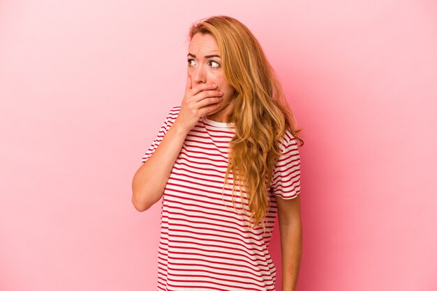 Femme blonde caucasienne isolée sur fond rose réfléchie à la recherche d'un espace de copie couvrant la bouche avec la main.