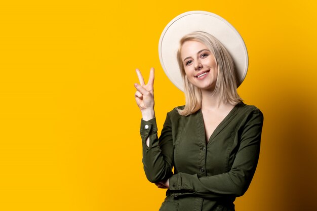 Femme blonde en chapeau et chemise verte sur mur jaune