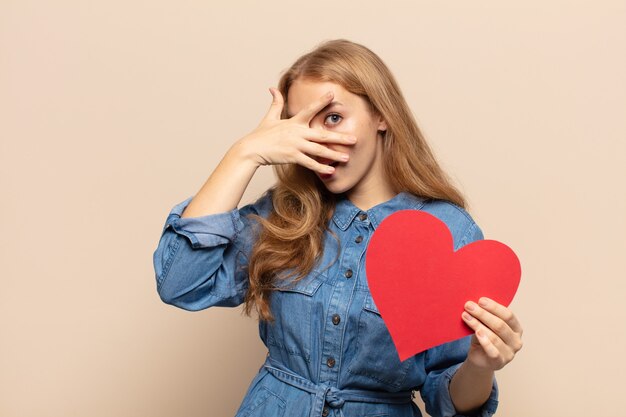 Femme blonde à la choqué, effrayé ou terrifié, couvrant le visage avec la main et furtivement entre les doigts