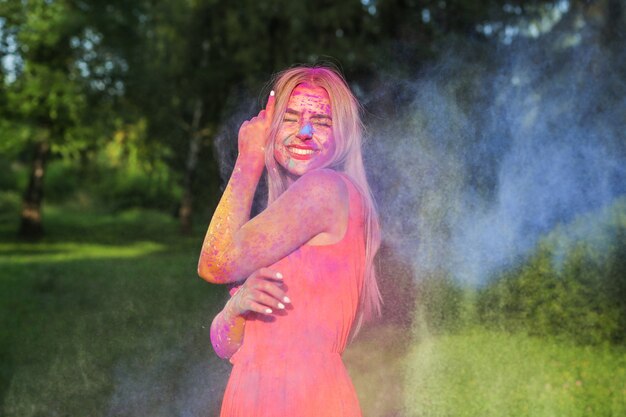 Femme blonde cool avec de la peinture colorée qui explose célébrant le festival Holi