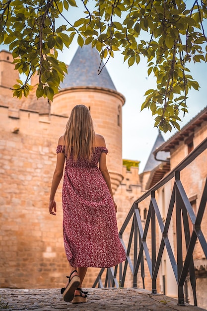 Femme blonde à côté d'un château médiéval avec une robe rouge par derrière