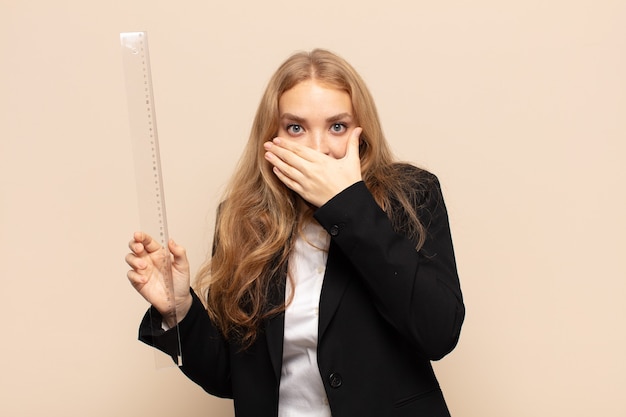 Femme blonde couvrant la bouche avec les mains avec une expression choquée et surprise, gardant un secret ou disant oups