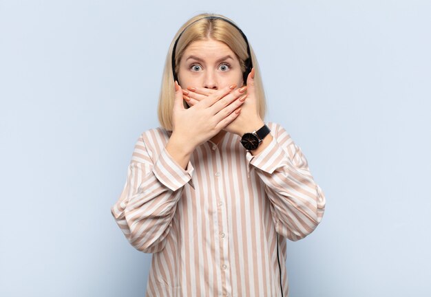 Photo femme blonde couvrant la bouche avec les mains avec une expression choquée et surprise, gardant un secret ou disant oups