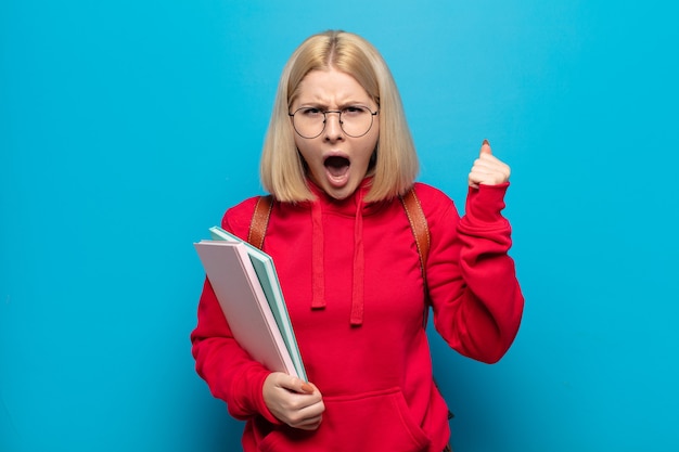 Femme blonde criant agressivement avec une expression de colère ou avec les poings serrés célébrant le succès