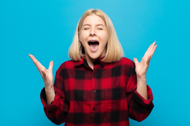 Femme blonde criant furieusement, se sentant stressée et ennuyée avec les mains en l'air disant pourquoi moi