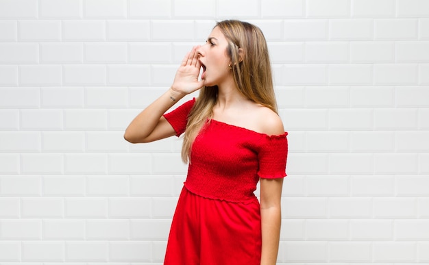 Femme blonde crier fort et en colère pour copier l'espace sur le côté, avec la main à côté de la bouche