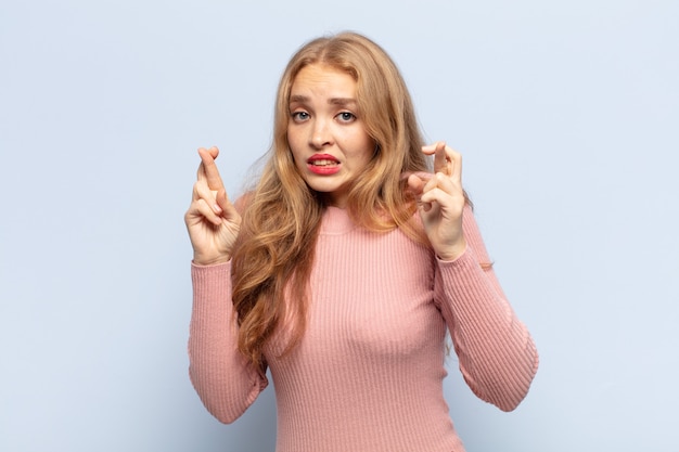 Femme blonde croisant les doigts avec impatience et espérant bonne chance avec un regard inquiet