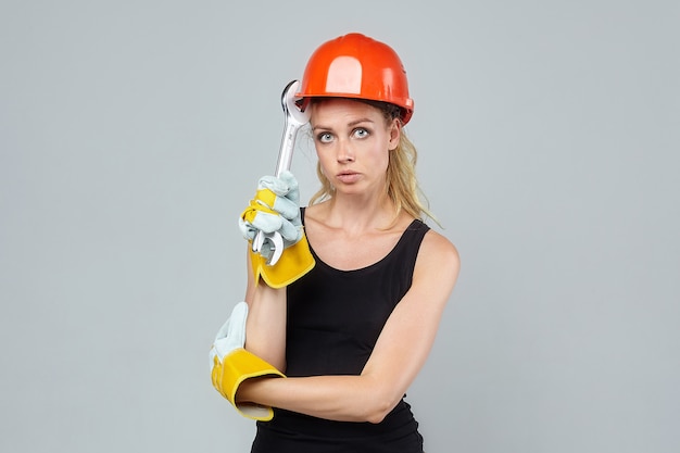 Femme blonde. dans un casque et des gants de protection, tenant une grosse clé.