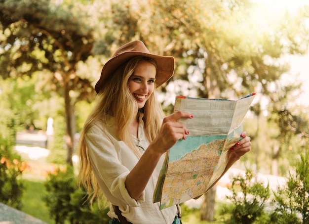 Femme blonde dans un chapeau de feutre regarde le plan de la ville et se promène dans une ville inconnue en plein air