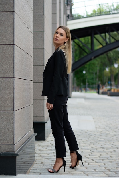 Une femme blonde dans un costume noir dans la ville.femme d'affaires sur une promenade.