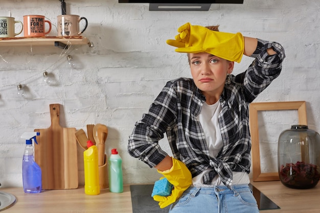 Femme blonde dans des gants de protection avec un chiffon nettoyant une cuisinière électrique à la maison cuisine fille lavant blac...