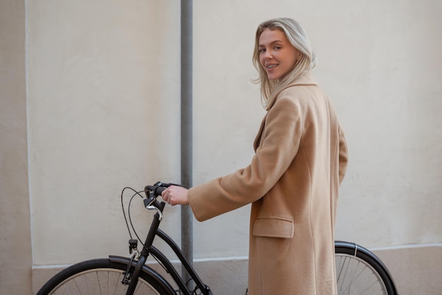 Femme blonde dans un manteau beige avec un vélo dans la rue