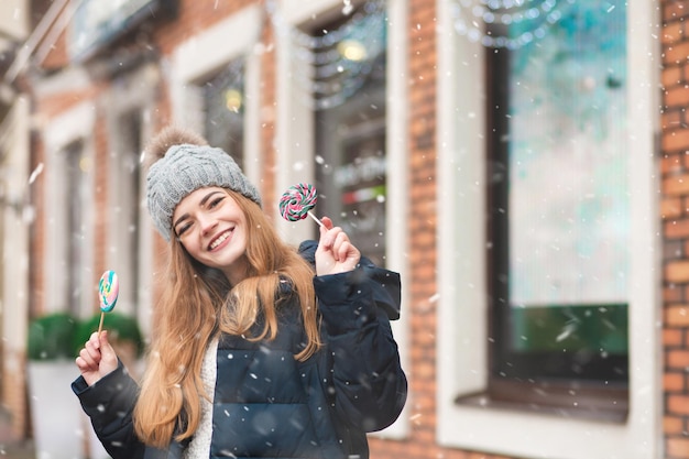 Femme blonde drôle profitant des vacances d'hiver avec une sucette colorée dans la rue. Espace libre