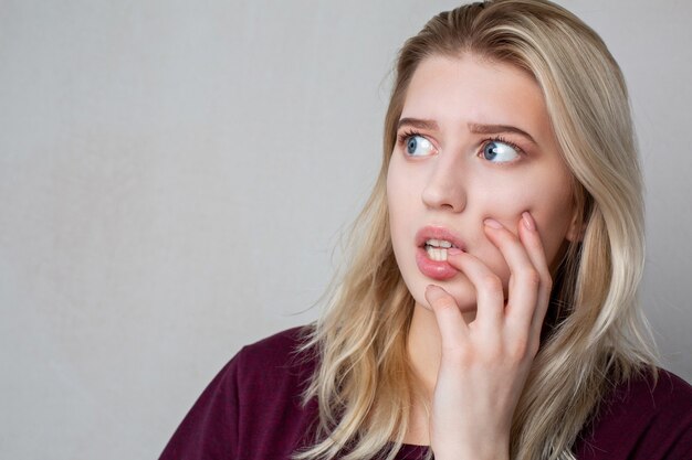 Femme blonde effrayée avec du maquillage naturel posant sur un fond gris. Espace libre